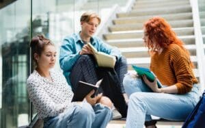 University students sitting on stairs and talking indoors, back to school concept